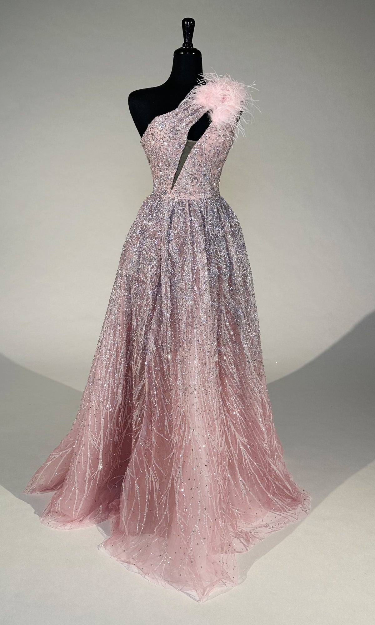 The Portia and Scarlett PS24411 Long Prom Dress is a blush pink, one-shoulder gown with sparkling sequins, a feather-accented strap, and a floor-length skirt—perfect for an unforgettable prom night.